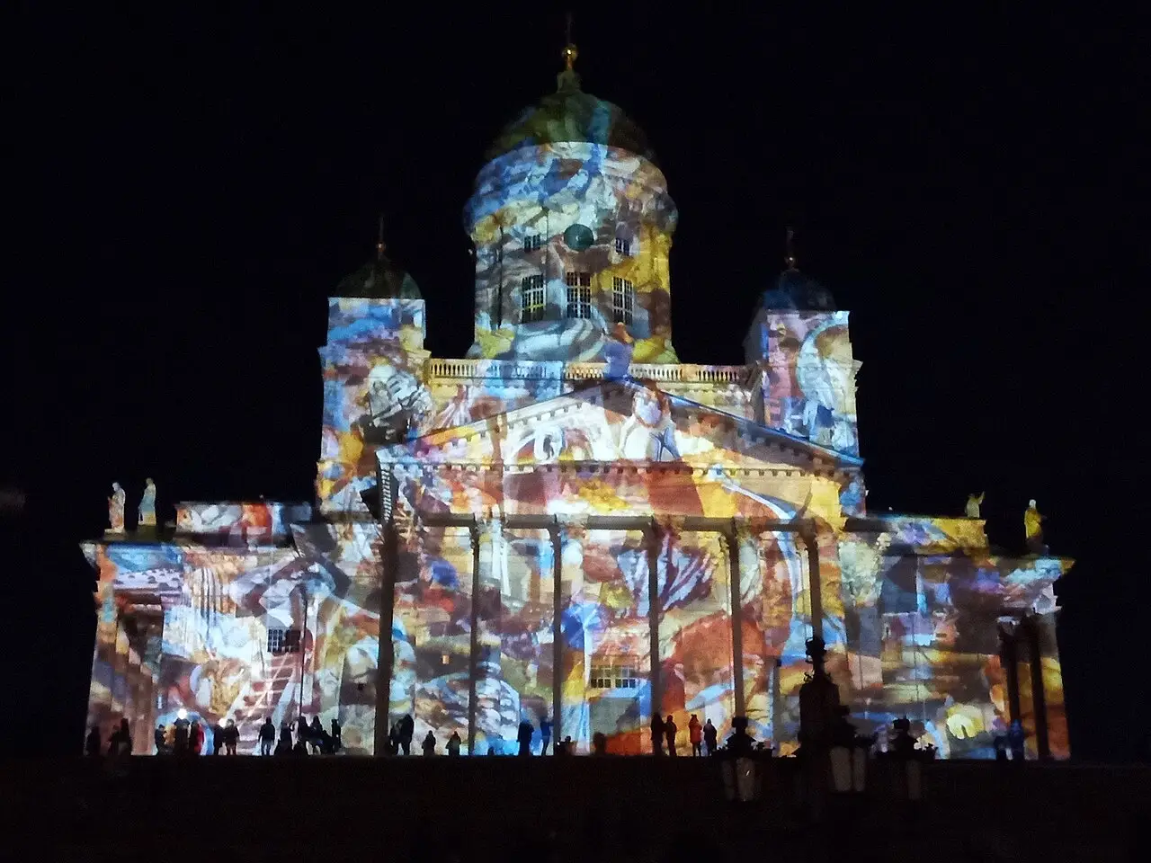 Fachada da Catedral de Helsinque coberta por projeções coloridas em movimento, à noite, durante o Lux Helsinki de 2020.