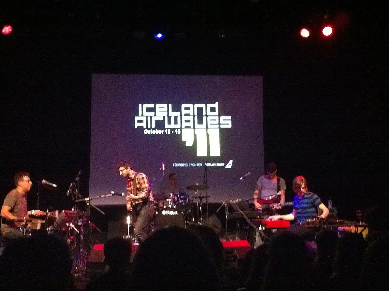 Banda tocando num palco escuro diante de um telão com o logotipo do Iceland Airwaves 2011, com luzes azuis e vermelhas.