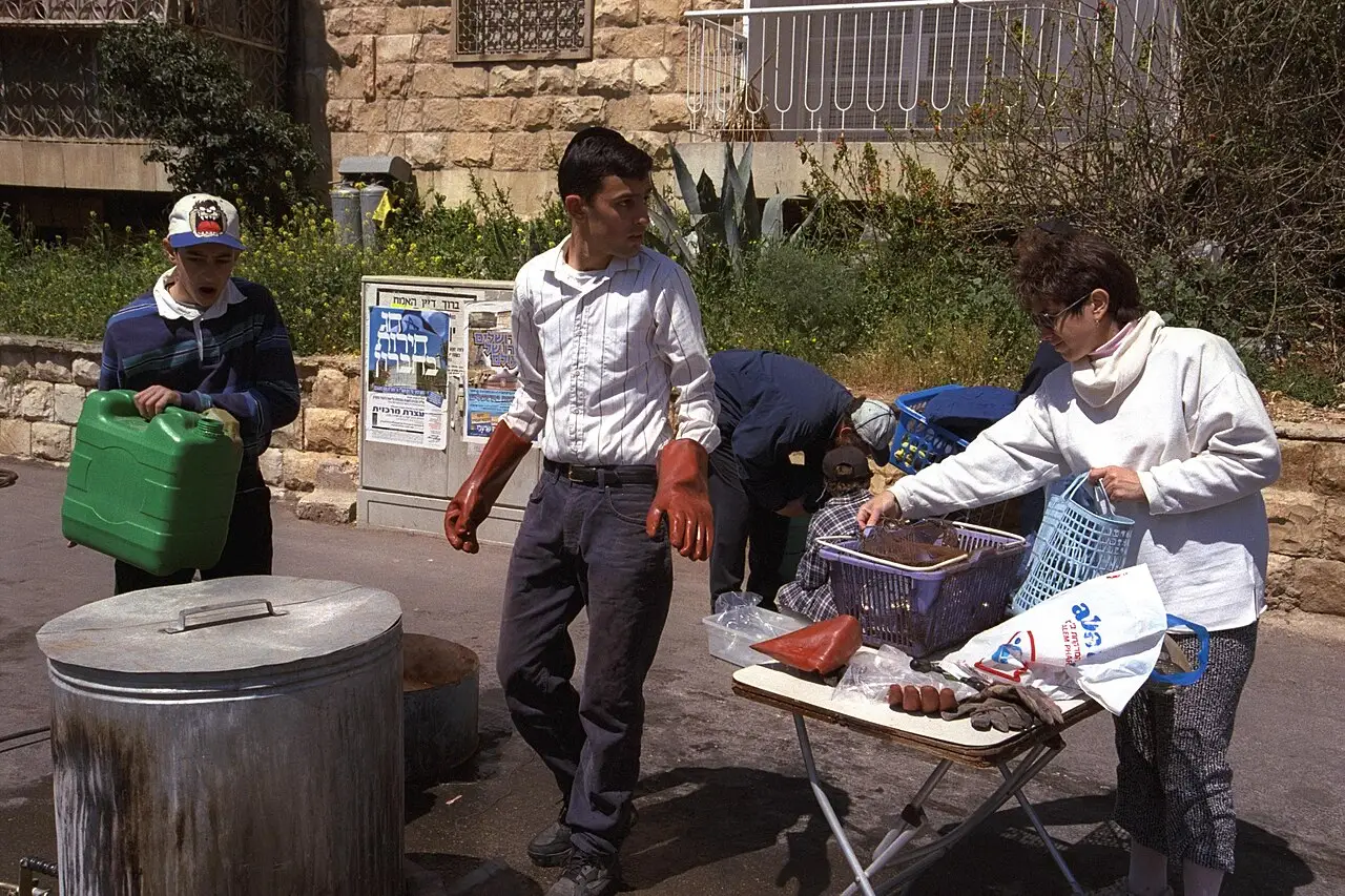 Homens preparando uma grande panela e utensílios ao ar livre, numa rua de Jerusalém, para a limpeza da louça antes do Pessach.
