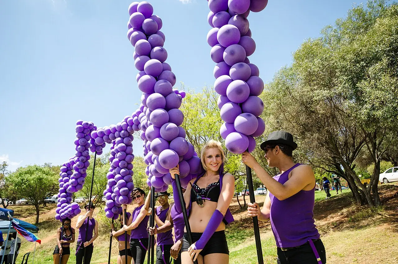 Participantes da marcha do orgulho carregando colunas altas de balões roxos num parque, sob céu azul, em 26 de outubro de 2013.