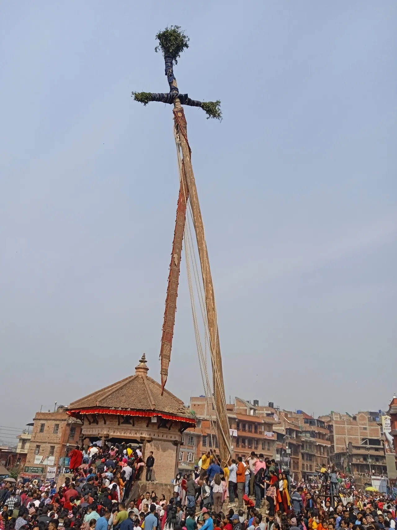 Um mastro muito alto, com ramos no topo e longas faixas de pano, erguido ao lado de um pavilhão de tijolo em Bhaktapur, no Bisket Jatra de 14 de abril de 2023.