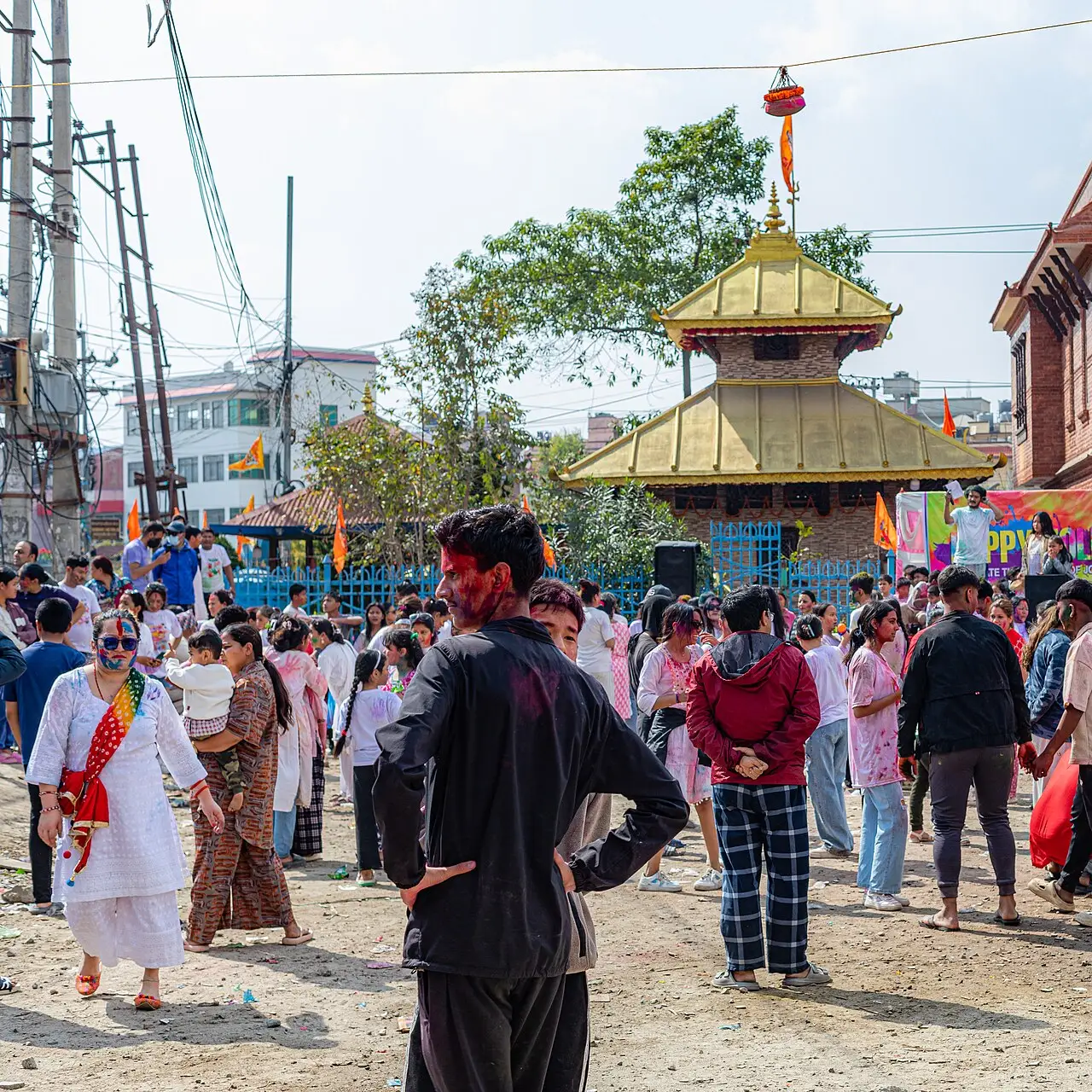 Multidão com pó colorido diante de um templo dourado durante o Holi em Katmandu, em 2025.