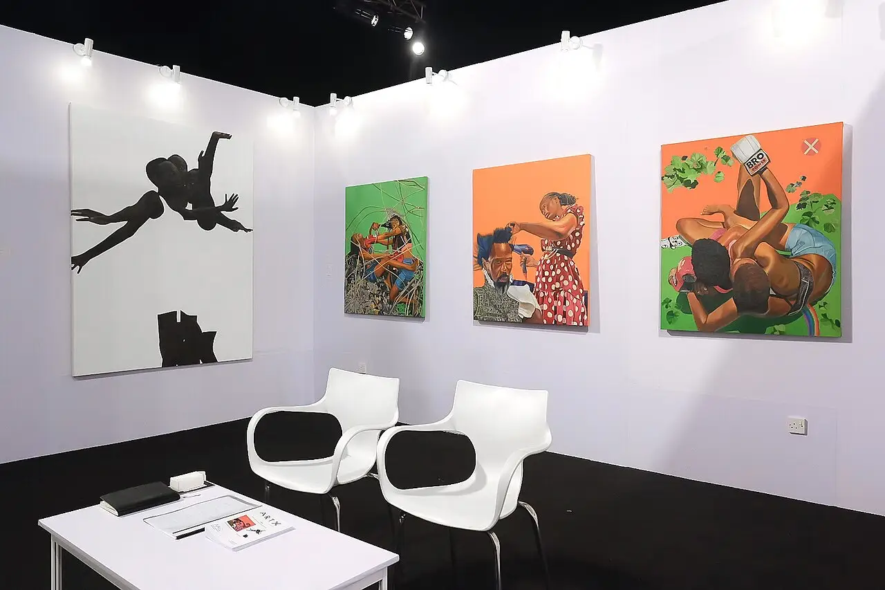 Estande da Afriart Gallery com quatro pinturas coloridas nas paredes brancas e duas cadeiras ao redor de uma mesa, na feira Art X Lagos de 2022.