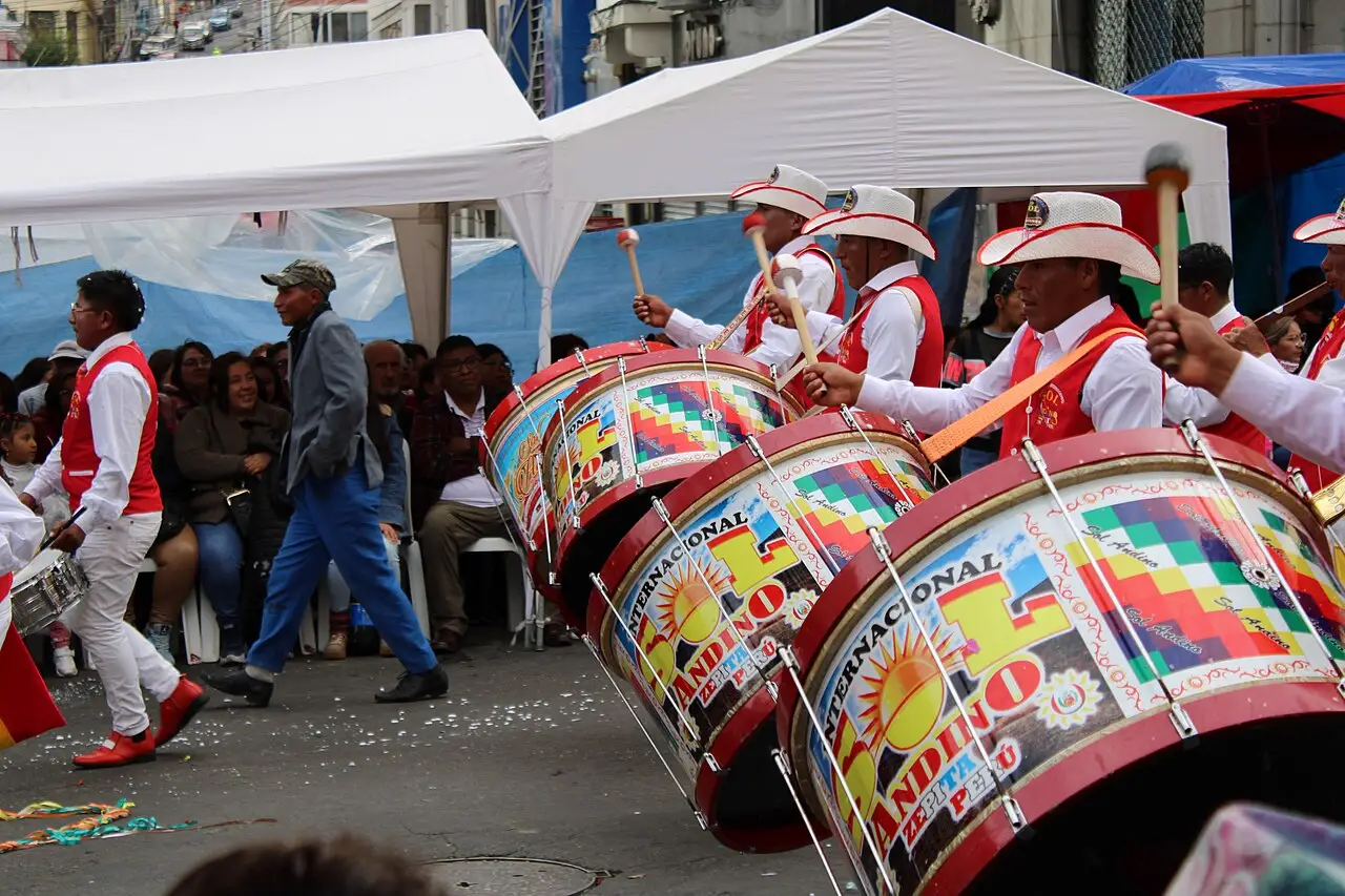 Tocadores de tambores grandes pintados com cores andinas, de chapéu e camisa vermelha, desfilando na rua durante o Jisk’a Anata em La Paz.