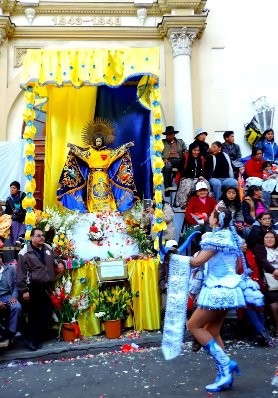 Imagem do Señor Jesús del Gran Poder sob um palio amarelo e azul, com flores, e uma dançarina de prata e azul ao lado, em La Paz, em 2015.