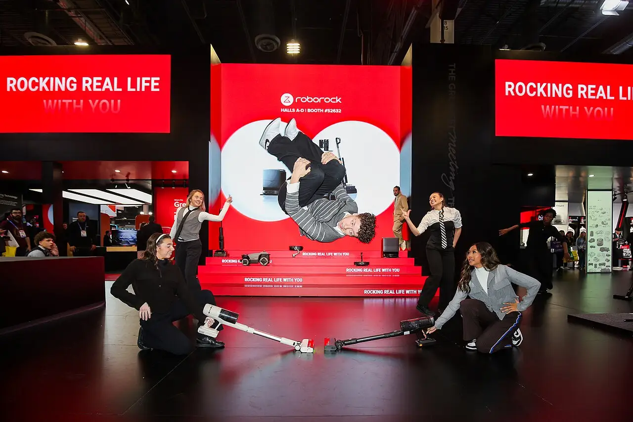 Grupo de dança se apresentando num palco vermelho, com painéis Roborock ao fundo, na feira de eletrônicos CES em Las Vegas.
