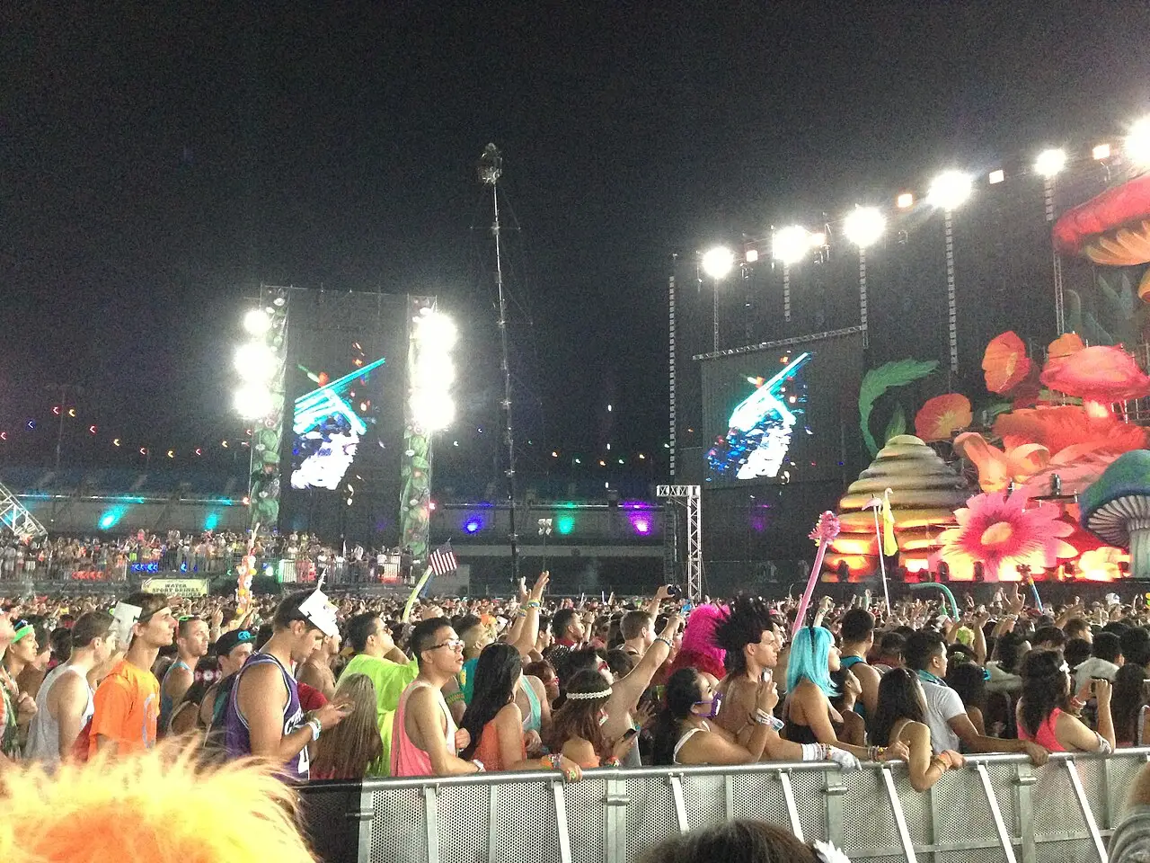 Multidão de jovens em trajes coloridos diante de um palco com telas e cenário iluminado, ao anoitecer, no Electric Daisy Carnival de 2013.
