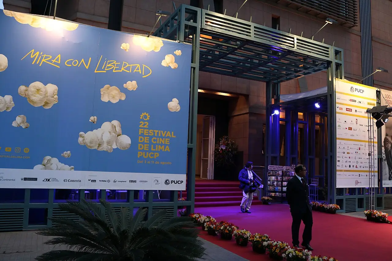 Entrada do Centro Cultural PUCP com tapete vermelho e cartaz de nuvens do Festival de Cine de Lima, à noite.