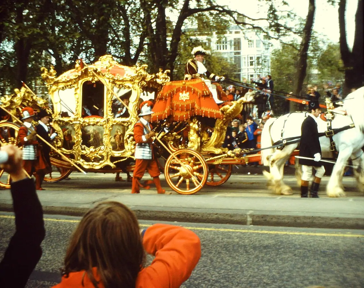 Carruagem dourada puxada por cavalos brancos passando por uma rua de Londres durante o Lord Mayor’s Show, com uma pessoa fotografando.