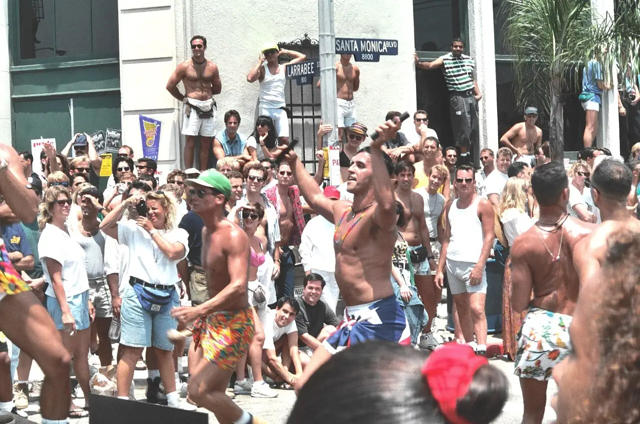 Multidão de pessoas, muitas sem camisa, reunida no cruzamento de uma rua de Los Angeles durante a parada LA Pride de 1993.