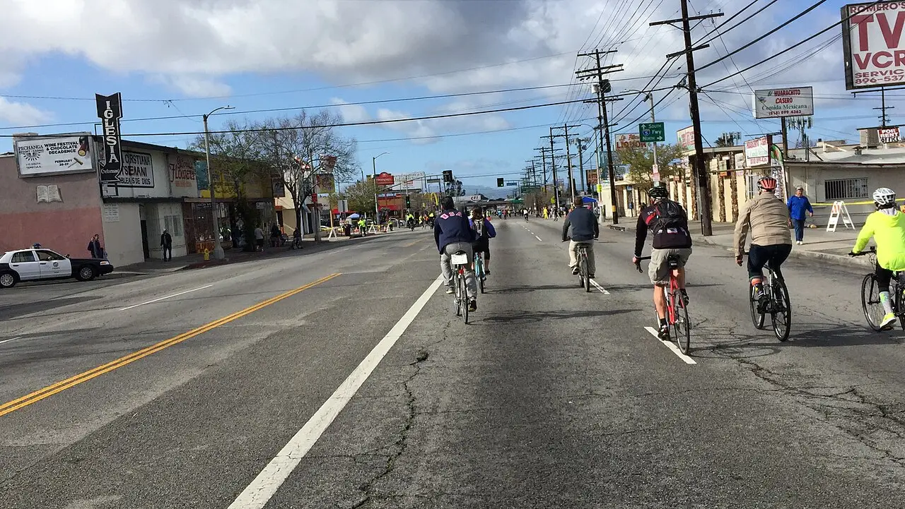 Ciclistas pedalando numa avenida larga sem carros, com fios de poste e comércio baixo dos lados, durante um dia de CicLAvia.