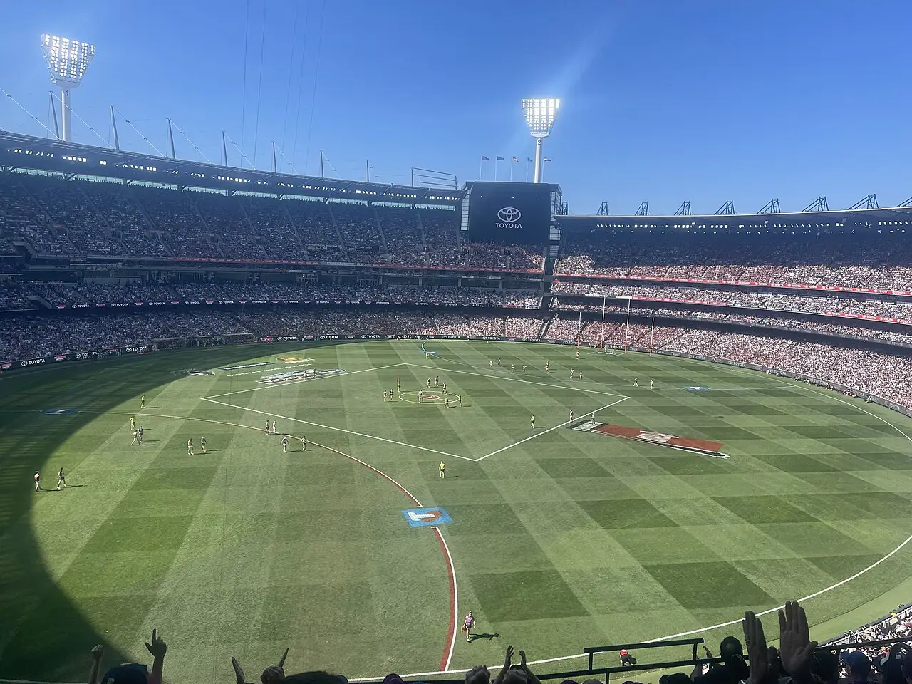 O estádio está lotado, jogadores estão no gramado e os holofotes cercam o campo.