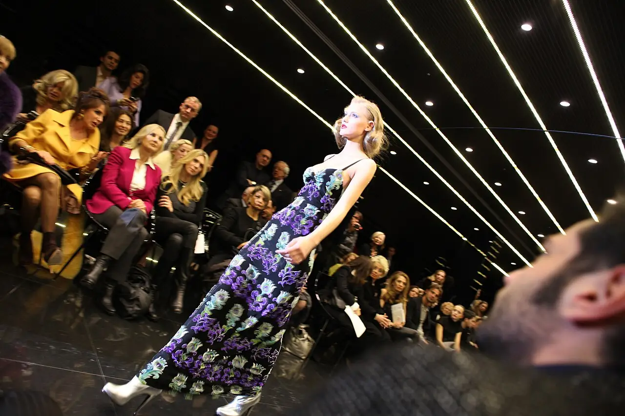 Uma modelo de vestido longo estampado caminha na passarela, com o público sentado dos dois lados.