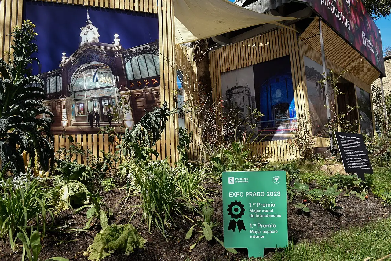Um estande de madeira traz o painel de um pavilhão, plantas na frente e a placa verde da Expo Prado 2023.