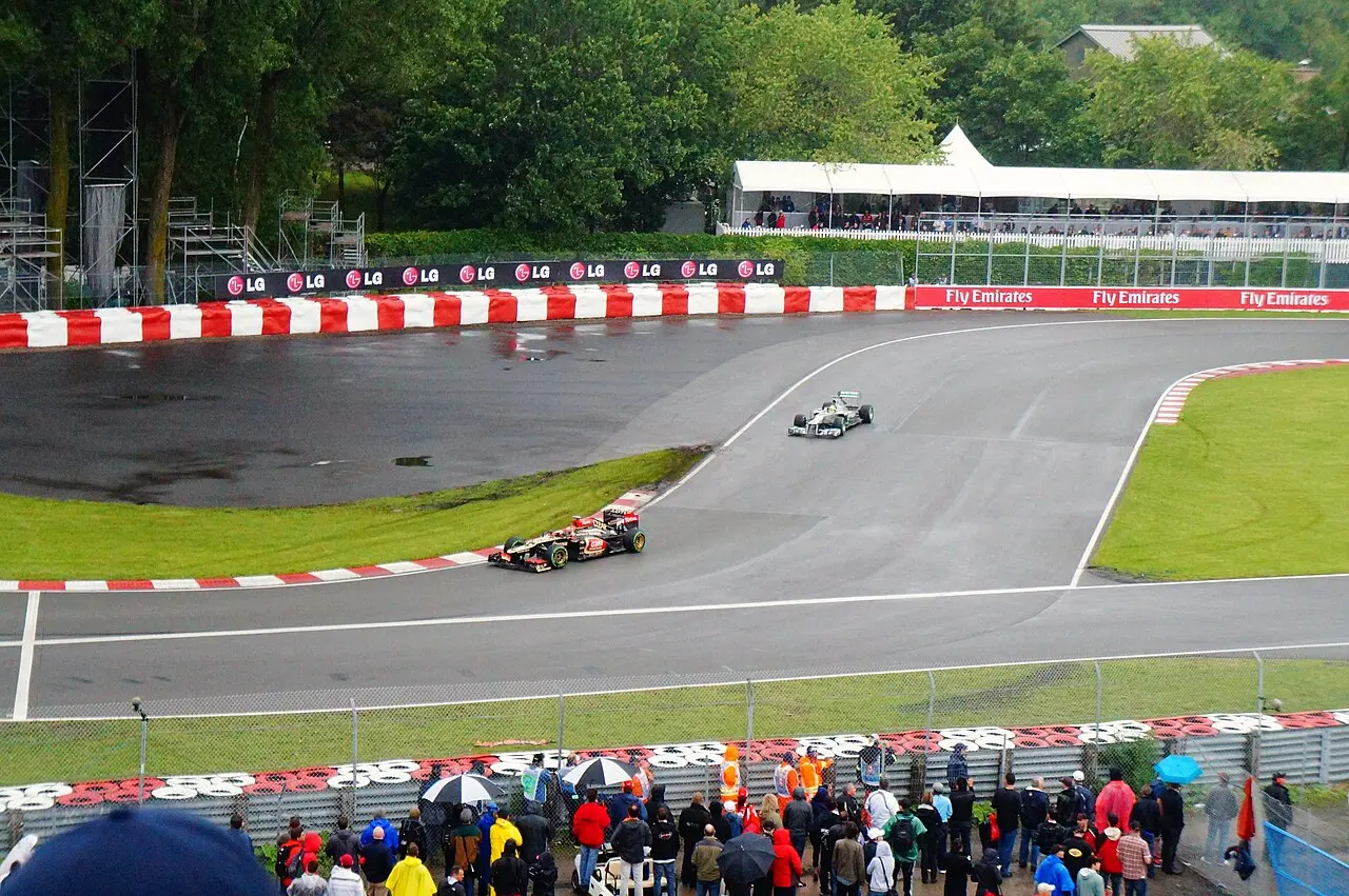 Carros de Fórmula 1 em uma curva do circuito Gilles-Villeneuve, com arquibancadas, barreiras e árvores ao redor, em 2013.