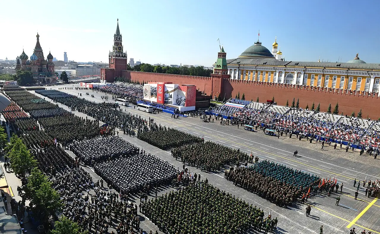 Blocos de tropas em formação ocupam a praça, com a muralha do Kremlin e a torre do relógio ao fundo.