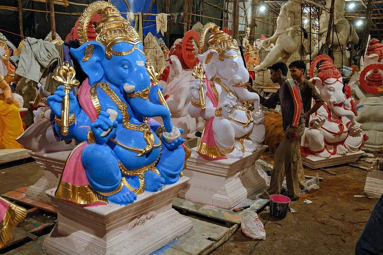 Num galpão, várias estátuas de Ganesha, a maior azul à frente, e um homem ao lado das menores.