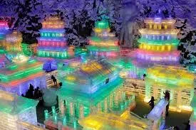 Pavilhões de gelo iluminados de verde, azul e laranja, com pinheiros ao fundo.