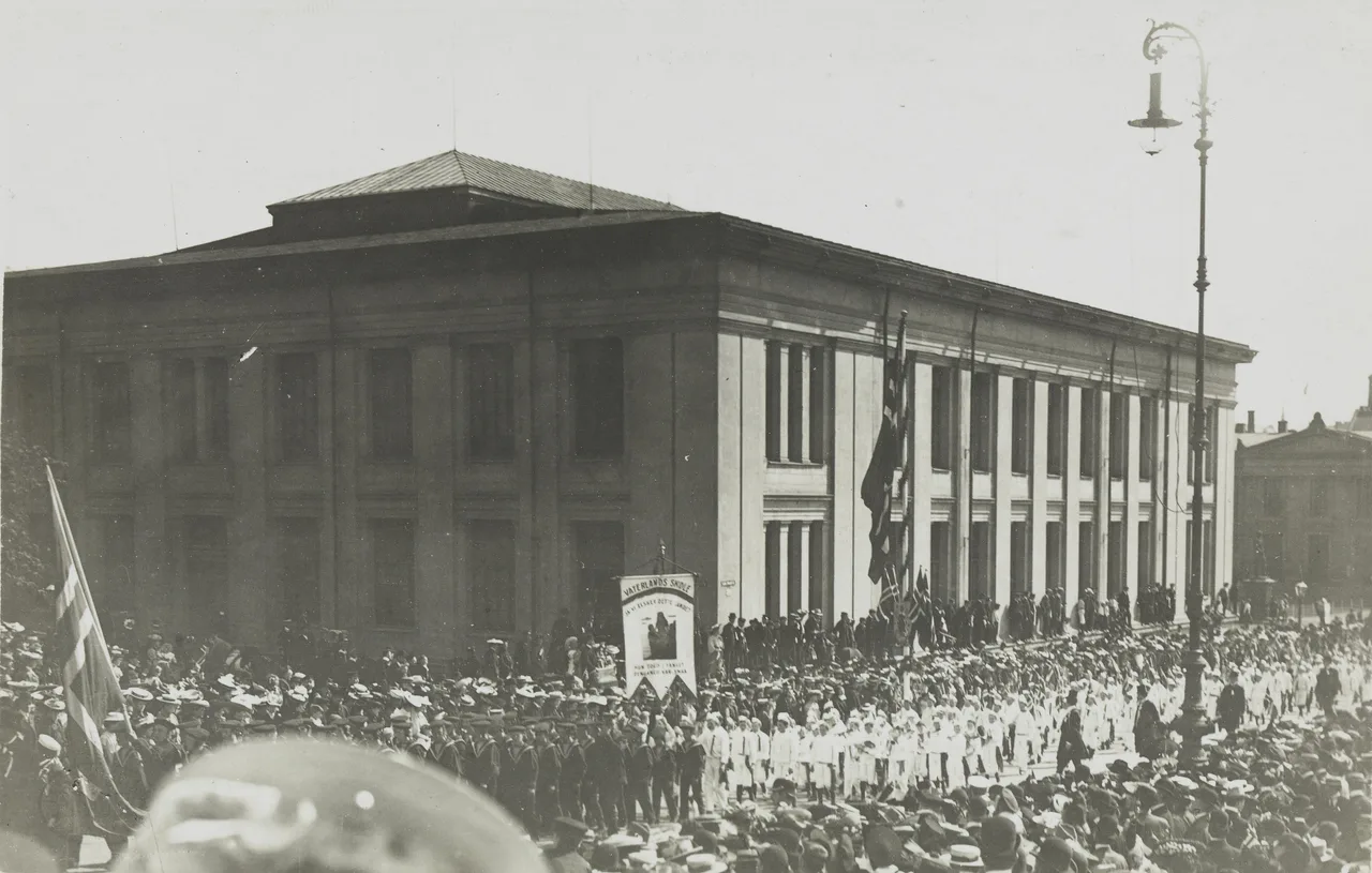 Cortège du 17 mai 1906 sur Karl Johans gate, devant l'université, avec des drapeaux norvégiens et une foule en chapeau.
