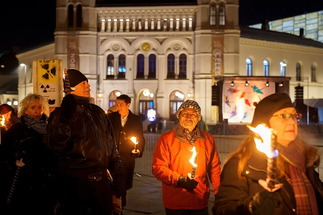 Des gens marchent la nuit avec des torches allumées devant un grand bâtiment clair aux fenêtres en arc.