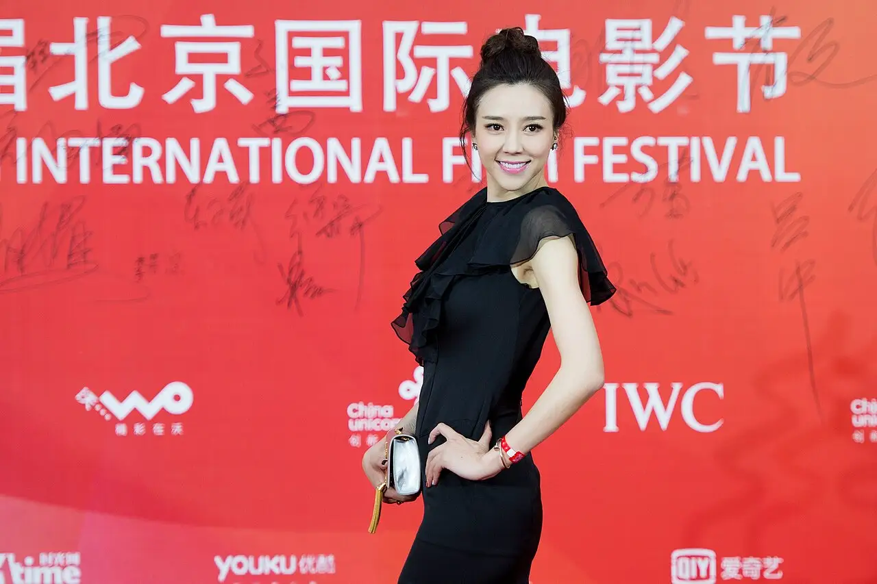 Uma mulher de vestido preto posa diante de um painel vermelho com o nome do festival de cinema.