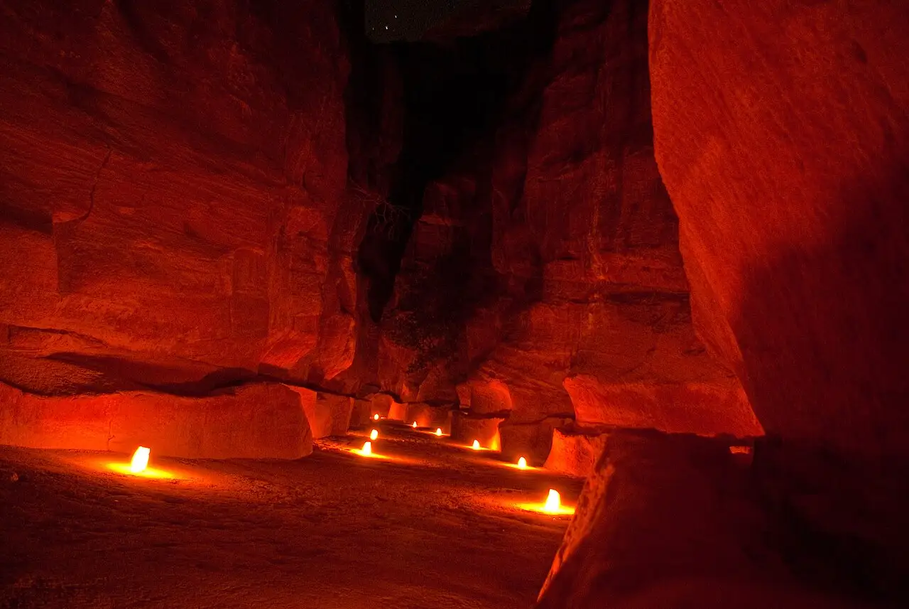 Velas acompanham a base das paredes de rocha vermelha do Siq, à noite.