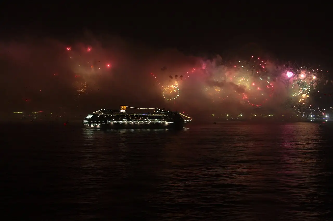 Fogos estouram sobre o mar, ao lado de um navio iluminado.