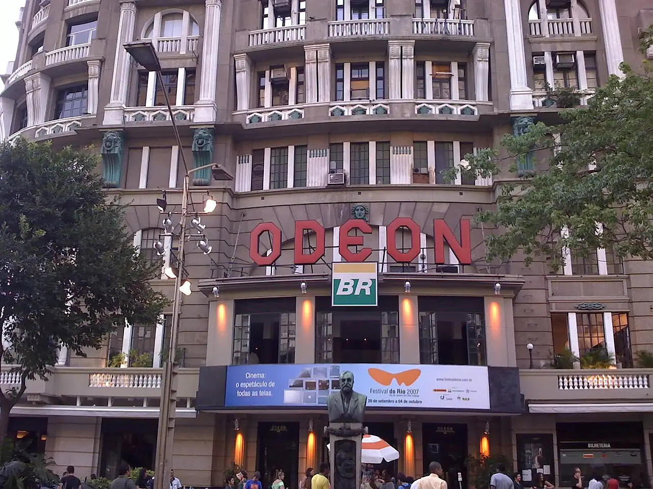 A fachada do cinema Odeon mostra as letras vermelhas, com gente na entrada e uma estátua à frente.