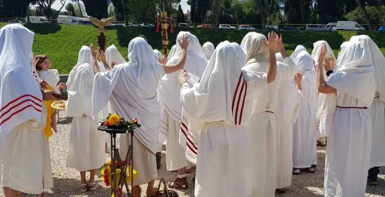 Des personnes en tunique blanche à bandes rouges sont réunies dehors autour d'un support bas.