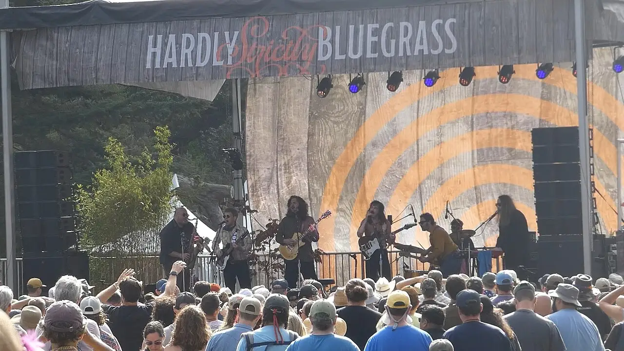 Uma banda toca num palco ao ar livre sob uma faixa que diz Hardly Strictly Bluegrass, com o público na frente.