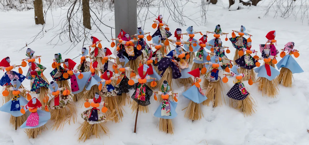 Dezenas de bonecos de palha com vestidos de tecido e fitas laranja estão fincados na neve.