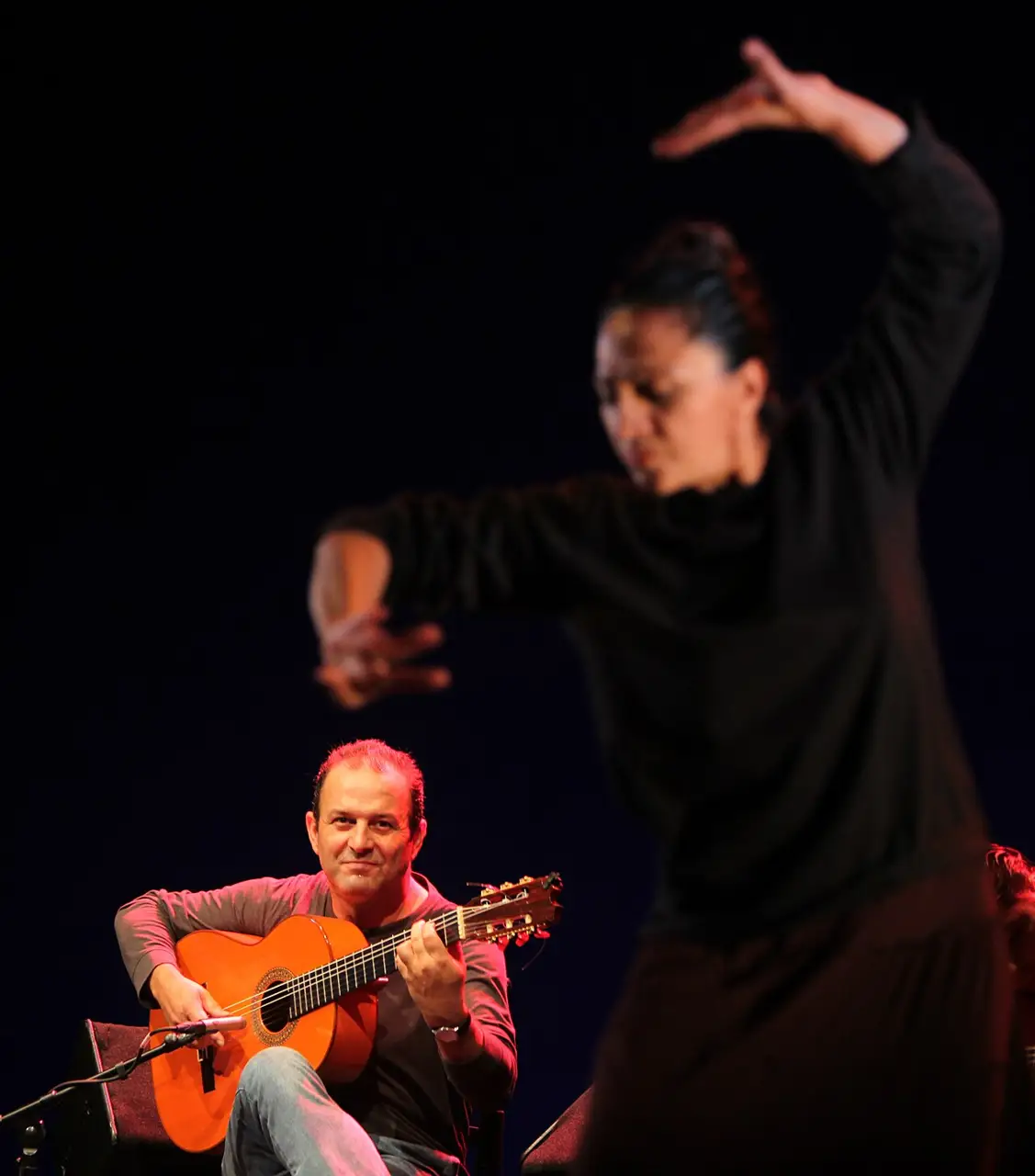 Guitarrista sentado e bailaora de preto com o braço erguido, no palco da Bienal de Flamenco de Sevilha, em 2012.