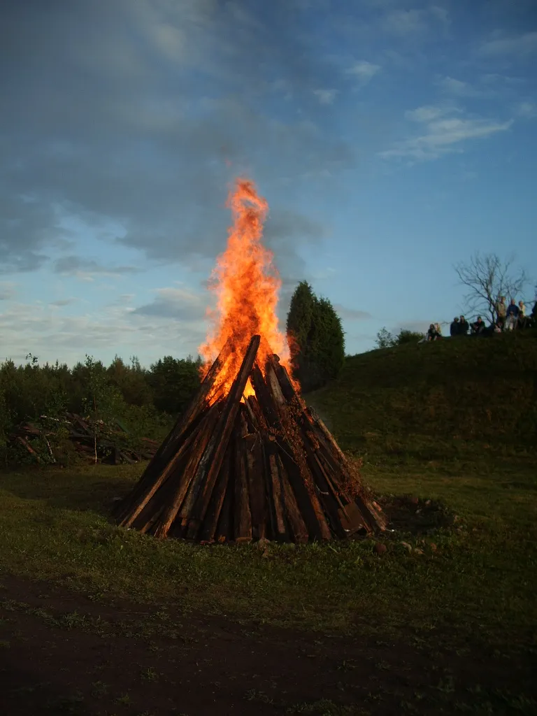 Uma fogueira de troncos em cone arde num campo de Valjala, na ilha de Saaremaa, na noite de 23 de junho de 2007, com um morro e árvores atrás.