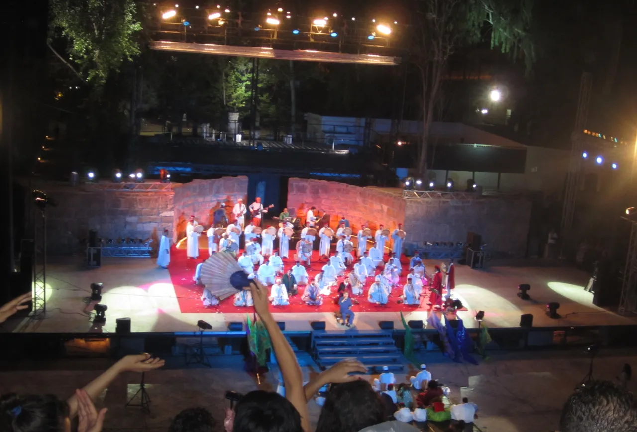 No teatro romano de Cartago, à noite, um grupo vestido de branco ocupa o tapete vermelho do palco, com leques e músicos ao fundo, no Festival de Cartago de 19 de julho de 2013.