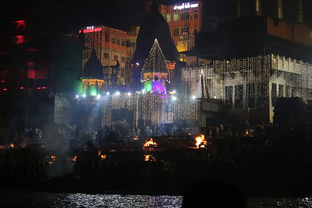 À noite, fileiras de luz e de fogo cobrem os degraus, com um templo iluminado ao fundo e a água na frente.