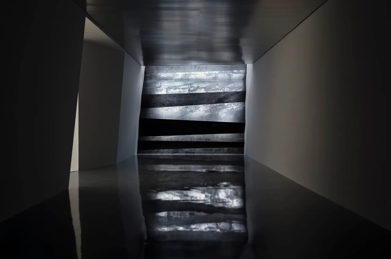 Um corredor escuro termina numa parede de painéis de tinta prateada e preta, a obra Wall of Skies na 11ª Bienal de Xangai.