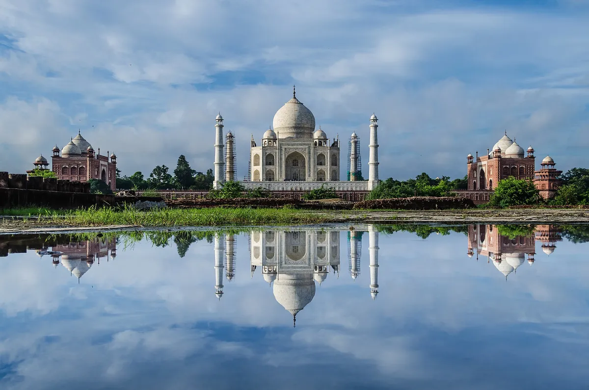 O mausoléu branco e os edifícios vermelhos dos lados, refletidos numa água parada.