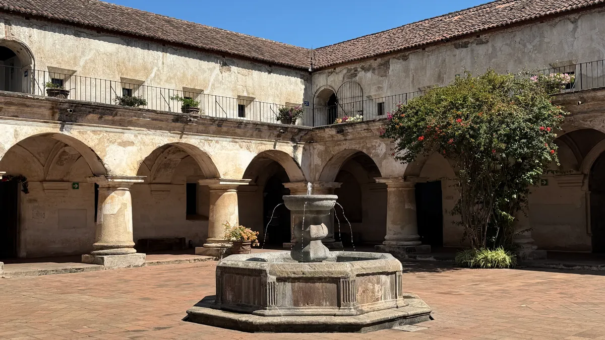 Pátio de pedra com fonte, arcos e telhado de telha.