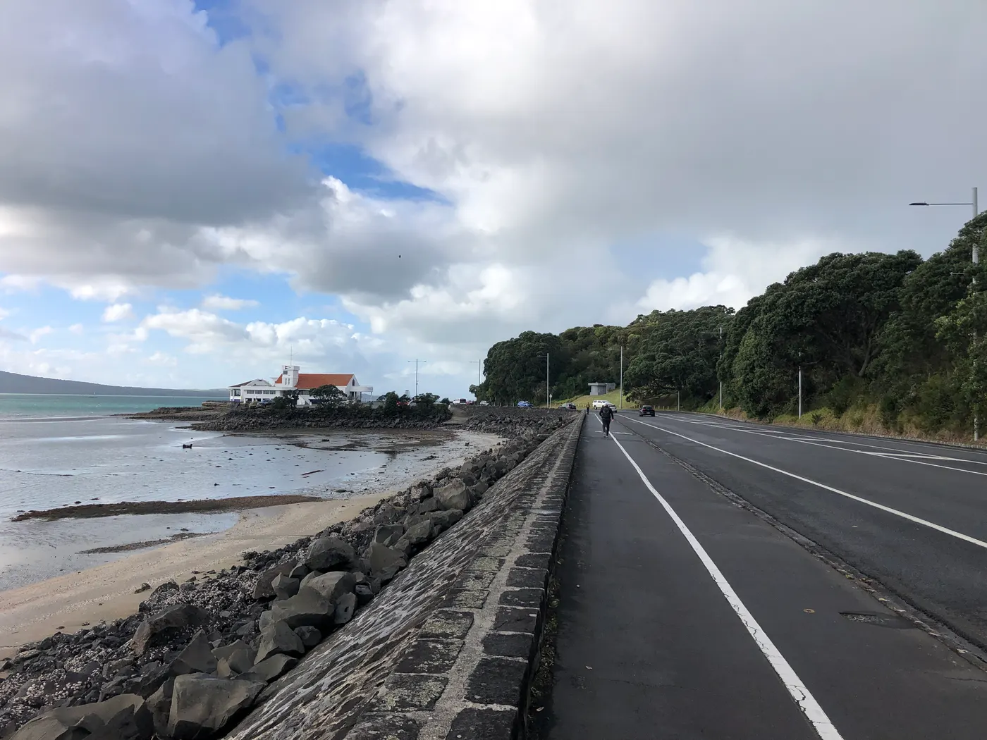Estrada à beira-mar, um clube branco de telhado laranja sobre as rochas e uma colina coberta de árvores.