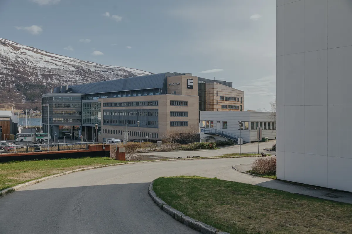 Edifício com o nome Framsenteret, fachadas de vidro e painéis claros, rua e montanha nevada ao fundo.