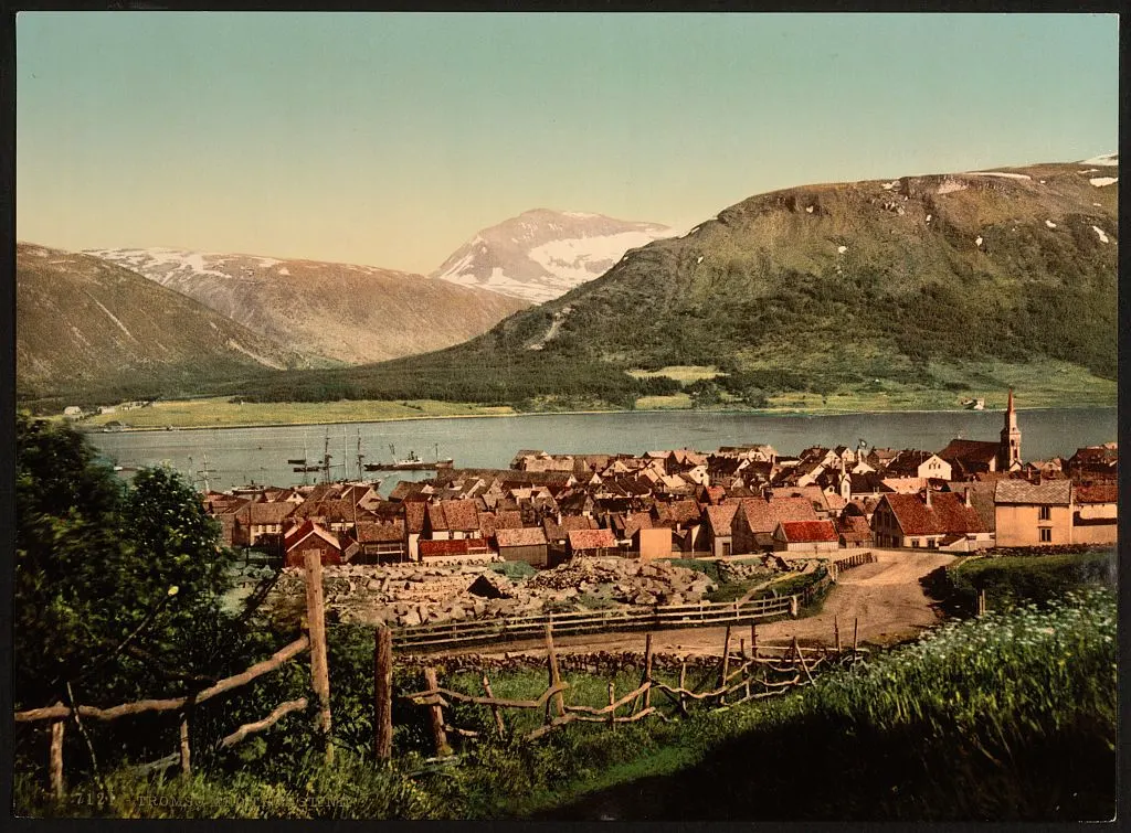 Vista colorida da cidade e do fiorde, com telhados, torre de igreja, mastros de barcos, cercas e montanhas ao fundo; borda e inscrição inferior preservadas.