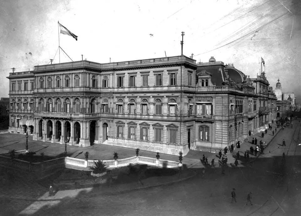 Fachada do palácio vista de cima, com arcos no térreo, uma bandeira no telhado e a praça em primeiro plano.