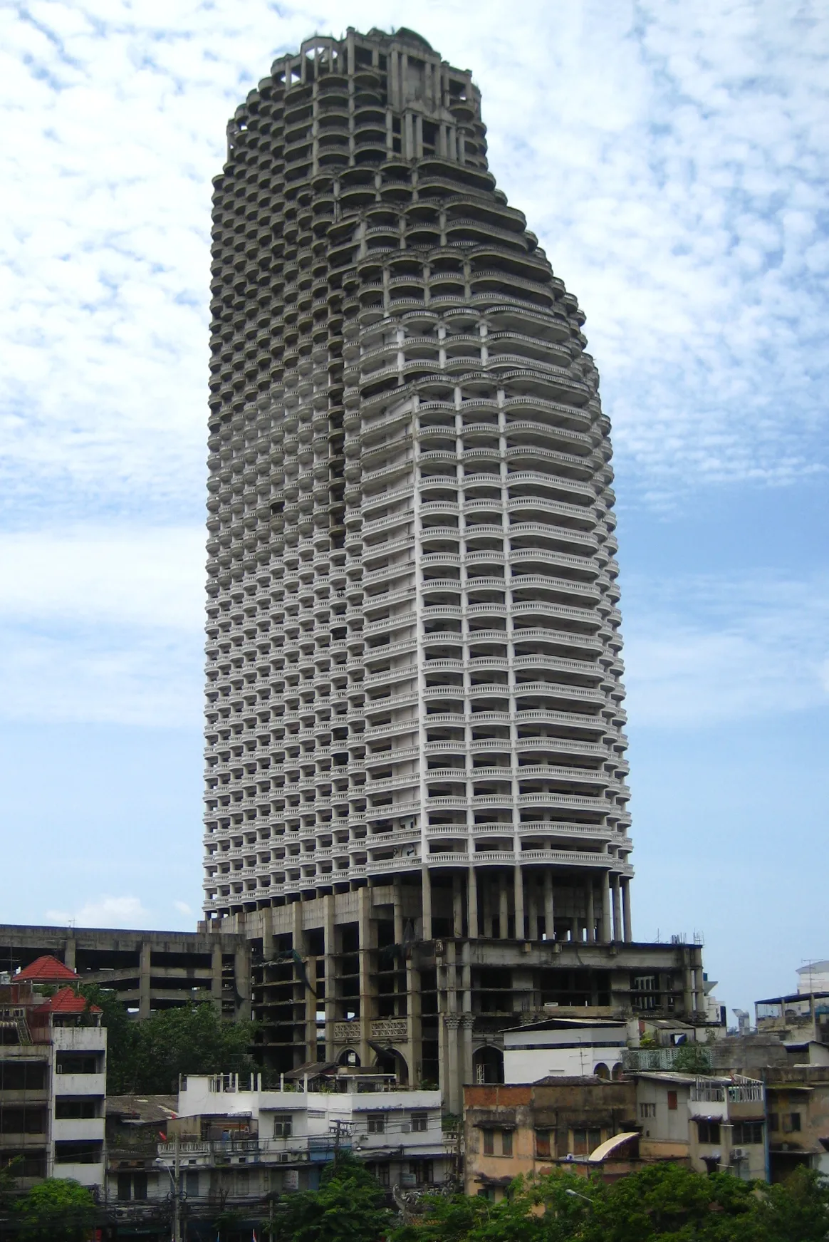Torre inacabada de concreto, com lajes abertas e sem fachada, acima de casas baixas.