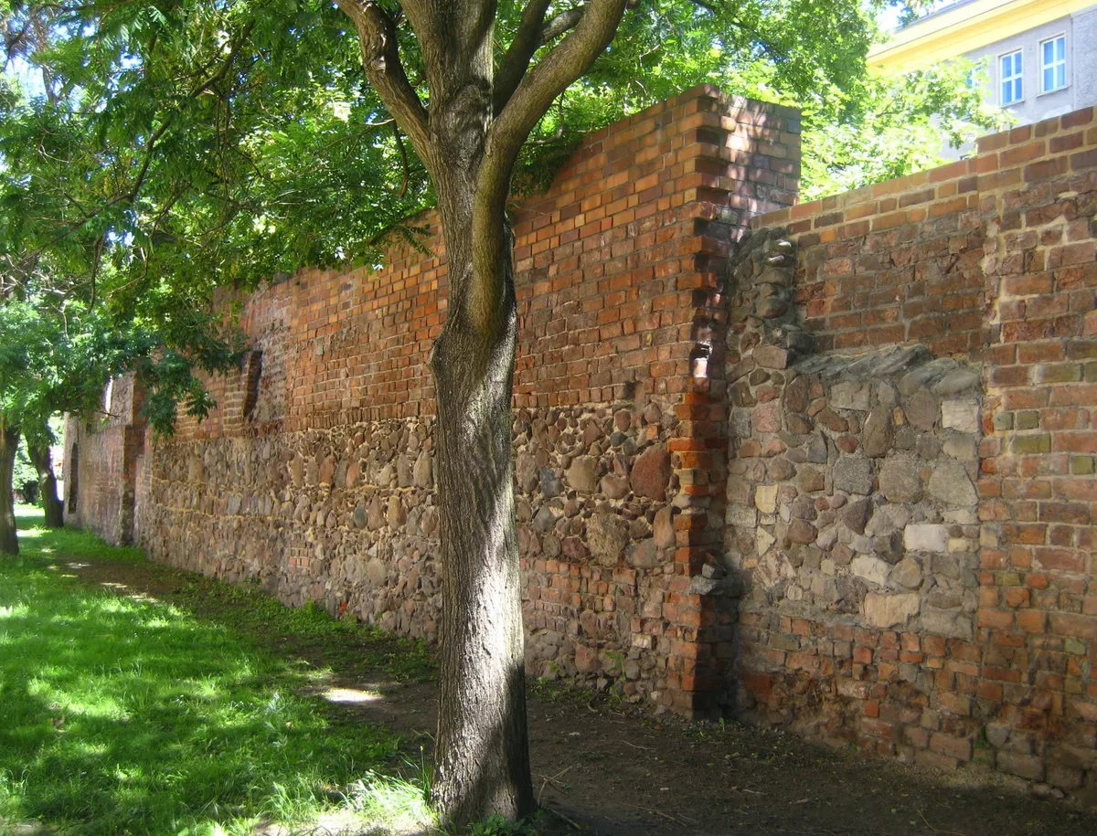 Trecho preservado da muralha entre Waisenstraße e Littenstraße, com pedras, tijolos, uma abertura e árvores.