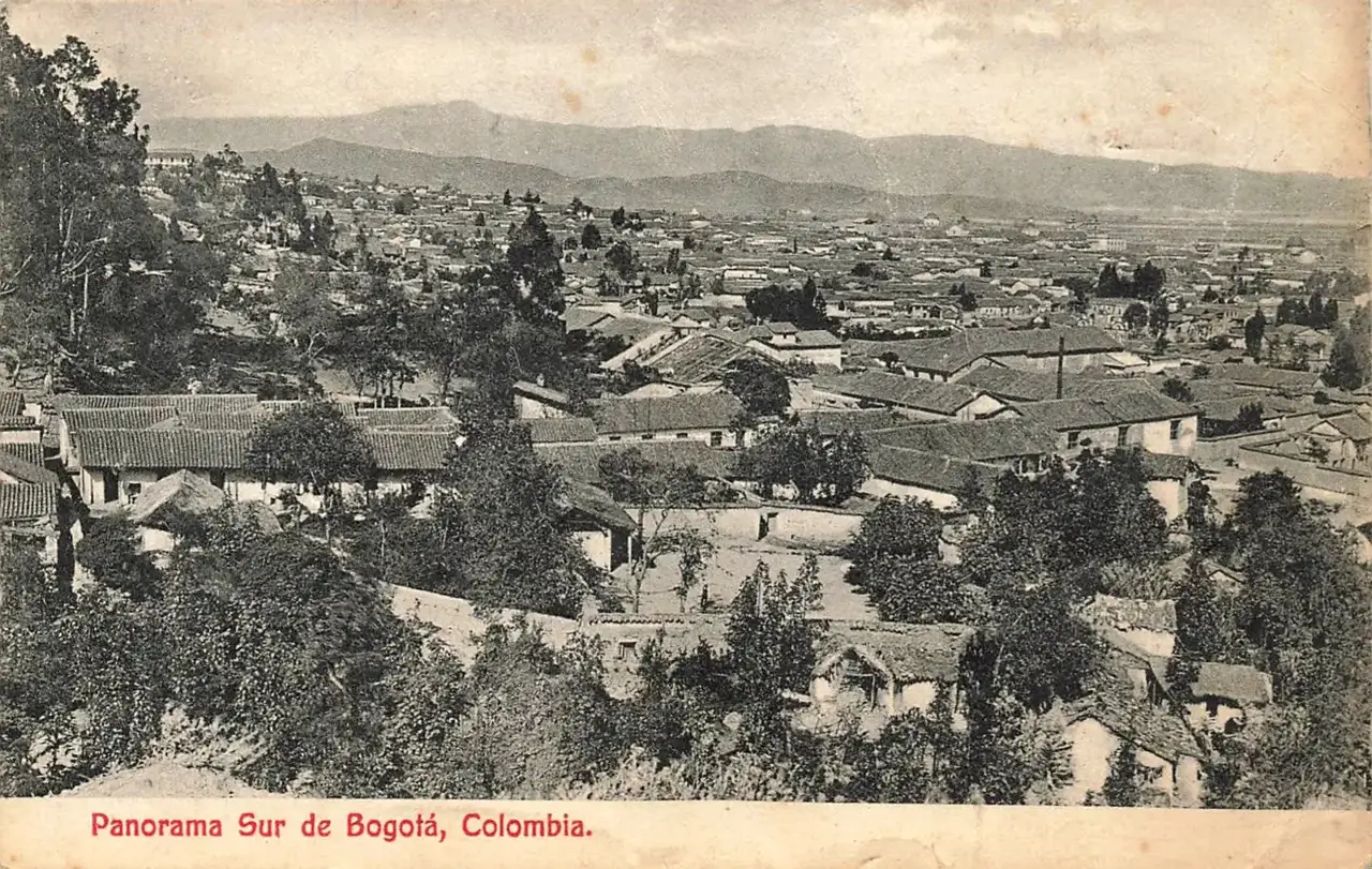 Cartão-postal em preto e branco com uma vista aérea de casas de telhado de telha entre árvores em Bogotá, montanhas ao fundo e a legenda impressa "Panorama Sur de Bogotá".
