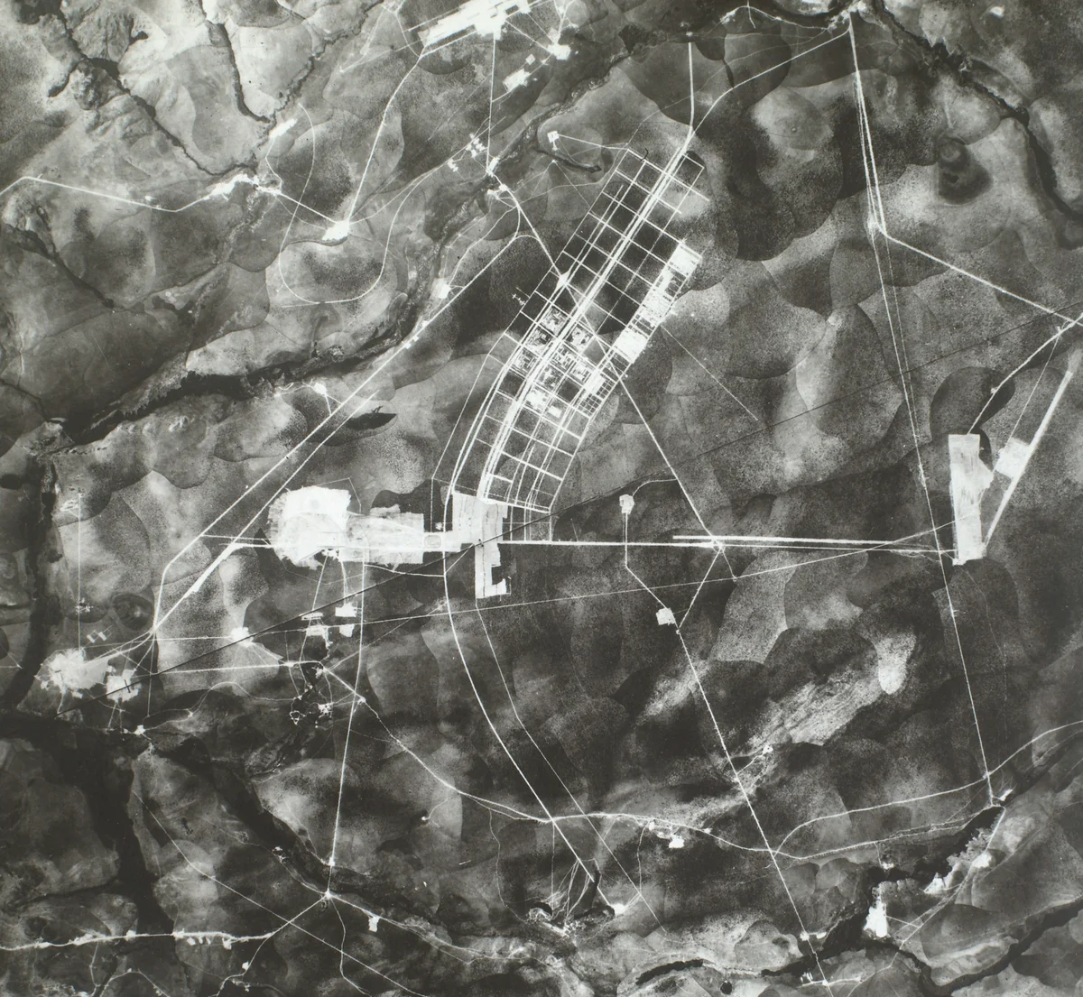Mosaico aéreo em preto e branco do Plano Piloto em construção, com eixos cruzados, quadras desenhadas e terreno aberto.