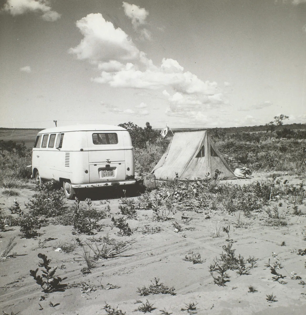 Barraca e Kombi estacionada num terreno aberto de cerrado, em fotografia em preto e branco dos preparativos da inauguração de Brasília.