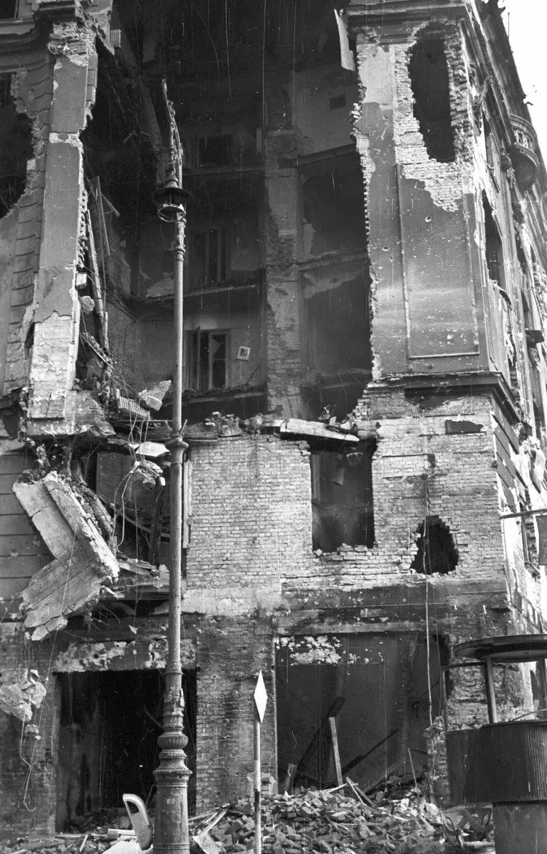 Fotografia vertical em preto e branco de um prédio com paredes abertas e andares danificados na esquina József körút–Üllői út, com um poste em primeiro plano.