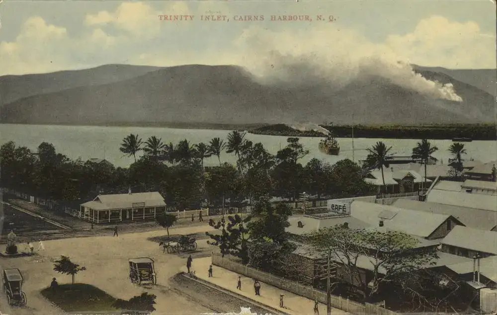 Cartão-postal colorido mostra Trinity Inlet, o porto de Cairns, visto de cima, com um navio a vapor na baía, casas de madeira, palmeiras e pessoas caminhando pela rua.