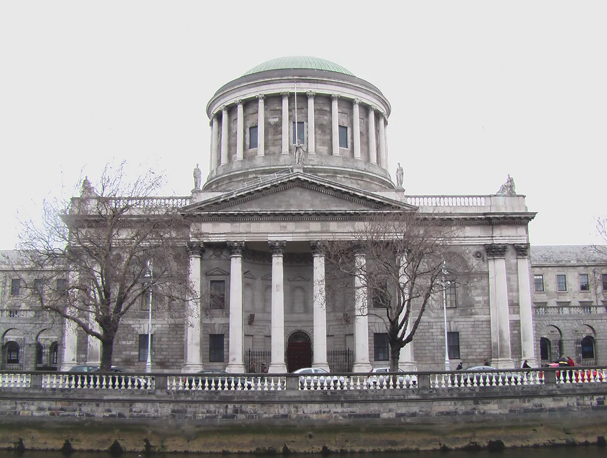 Four Courts façade seen across the Liffey, with dome, portico, columns, side buildings and trees.